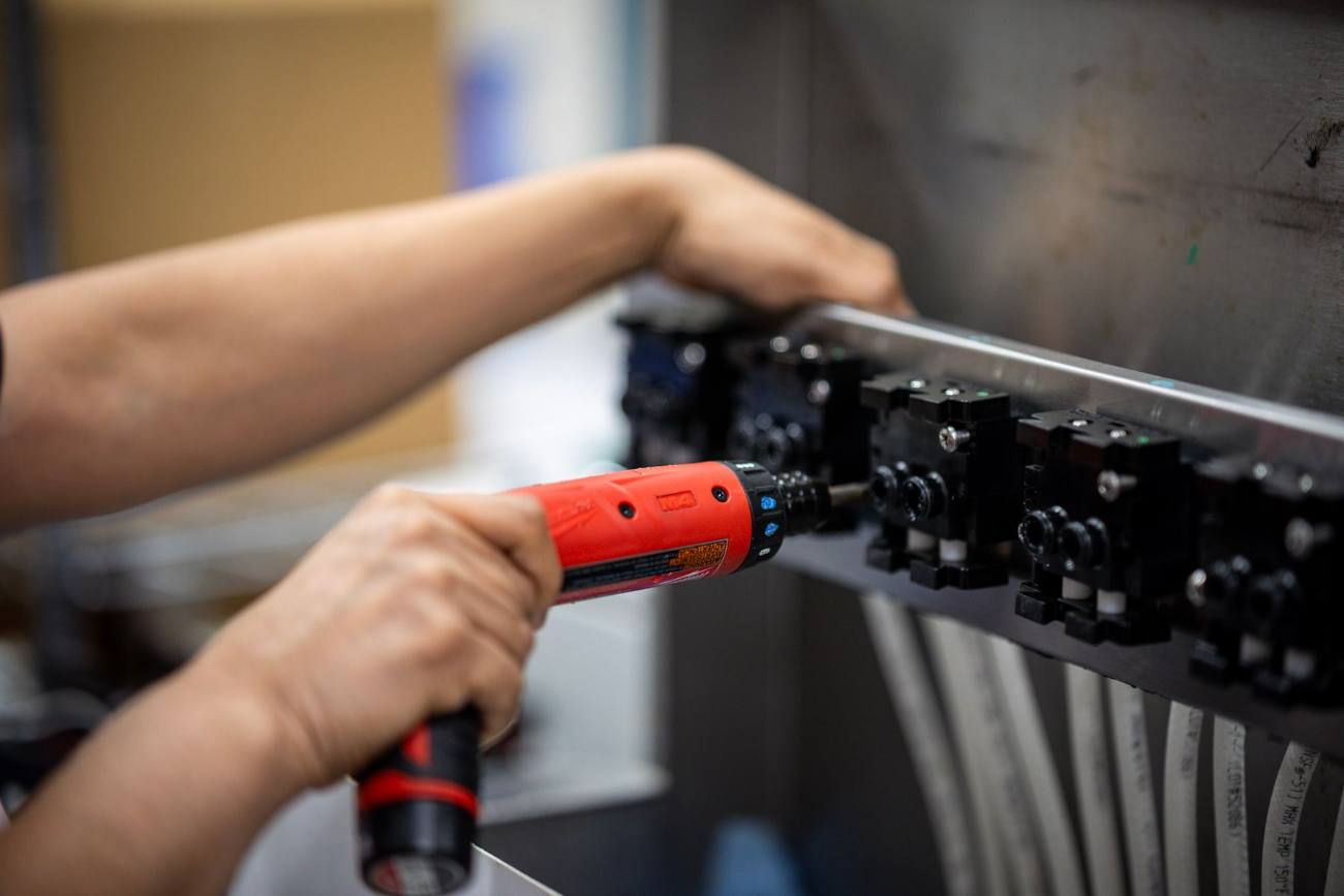 Close-up of a Marmon Renew technician's hands using a powered driver on a row of valves during remanufacturing